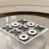 acrylic tic tac toe game set with black glitter X pieces and white O pieces displayed on a clear board, styled on a round glass coffee table in a contemporary living room