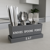 Gray cutlery organizer with labeled sections for knives, spoons, and forks on a kitchen counter.
