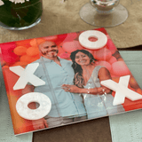 Personalized Photo Tic tac toe engagement photo on a table next to vase of flowers, pieces and colors are customizable