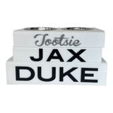 three solid white personalized pet bowls , Tootsie in grey script acrylic lettering, JAX and DUKE in black acrylic lettering.