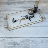acrylic be you tiful luxe tray with the word be you tiful in script, on a wooden table with beauty products displayed on it