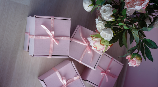 An arrangement of elegantly wrapped pink gift boxes with ribbons on a wooden floor, inspiring luxurious ideas for '10 Gifts the Woman Who Has Everything'.