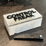 remote control box with clear lid that says CONTROL FREAK in double layer letters displayed on a coffee table.