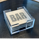 acrylic coaster set in white with the words BAR written in silver sparkle featured on a side table.