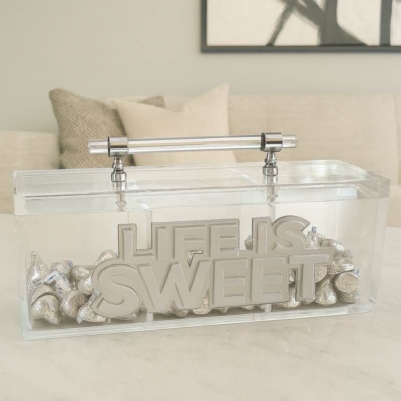 clear acrylic candy canister with bold letters that read LIFE IS SWEET in white and clear mirror filled with candy displayed on a living room table. A perfect personalized luxury acrylic decor piece and custom gift idea for modern homes, candy lovers and special occasions.