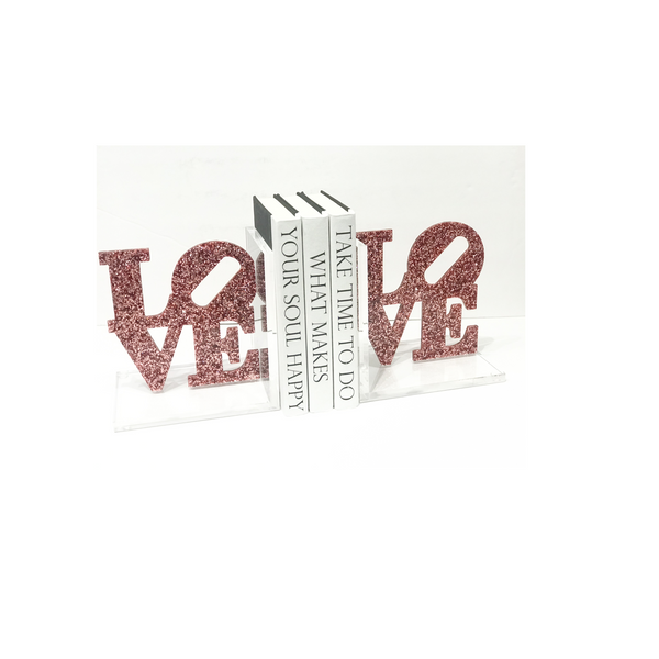 Custom acrylic bookends that spell LOVE in pink sparkle finish, styled on a shelf holding books