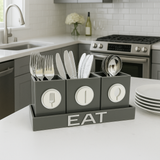 Gray utensil holder with cutlery on a kitchen counter, featuring the word 'EAT'.