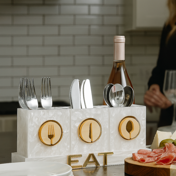 Marble utensil holder with cutlery on a kitchen counter, featuring a bottle of wine and charcuterie.