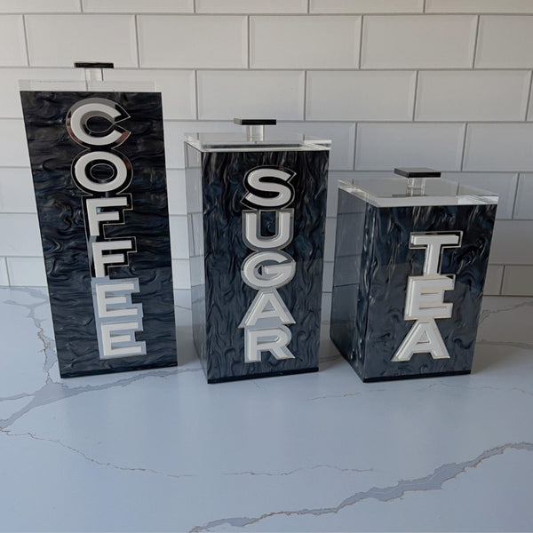 coffee corner acrylic canisters with lids on a kitchen counter that say COFFEE SUGAR and TEA in double layer letters