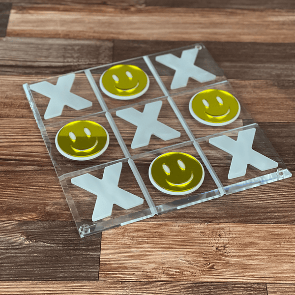 acrylic tic tac toe set with smiley mirror faces & white marble X pieces on a coffee table